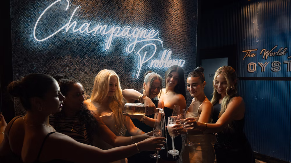 Guests pouring champagne beneath the Champagne Problem neon sign