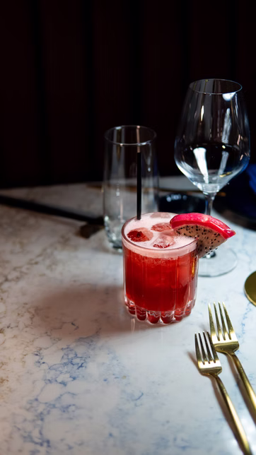 A red cocktail garnished with dragon fruit on a marble table
