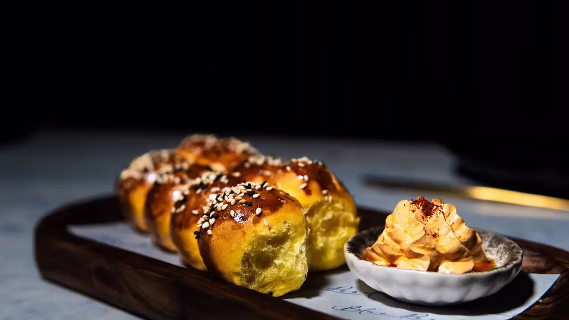 Sesame milk bread rolls with whipped chili butter on a wooden board