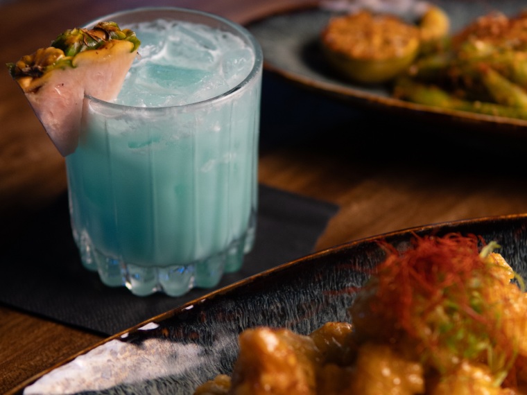 A pale blue cocktail garnished with charred pineapple