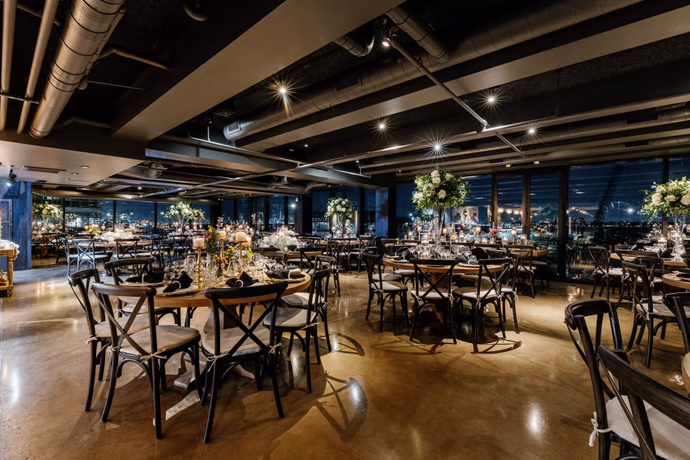 The Loft dressed for an event, round tables with tall floral centrepieces and the waterfront beyond