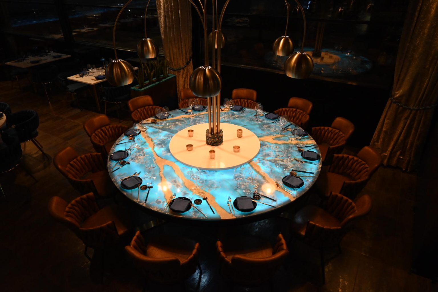 The Pearl set for twelve, its illuminated turquoise surface glowing beneath brass arc lamps